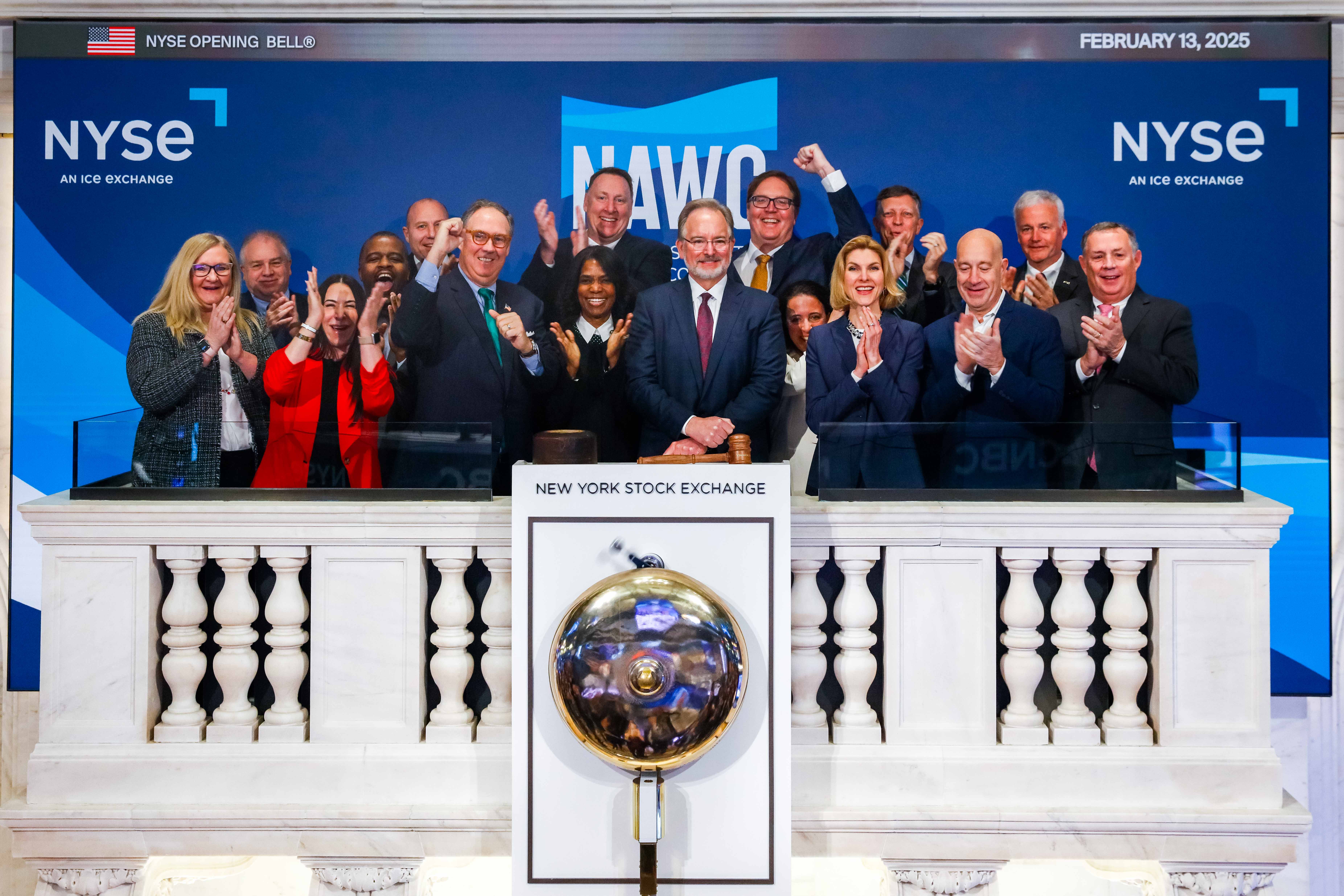 Martin A. Kropelnicki and other team members standing behind the New York Stock Exchange bell. 